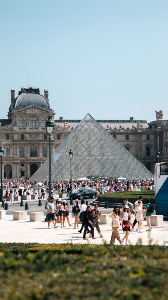 Massive tourist crowds waiting in line outside the Louvre glass pyramid entrance in Paris.
